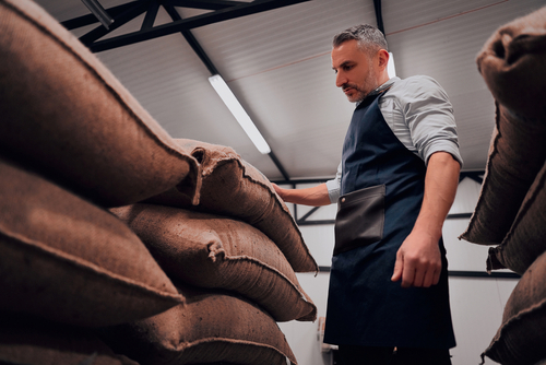 Roastery,Worker,Standing,At,Pile,Of,Sacks,With,Coffee,Beans